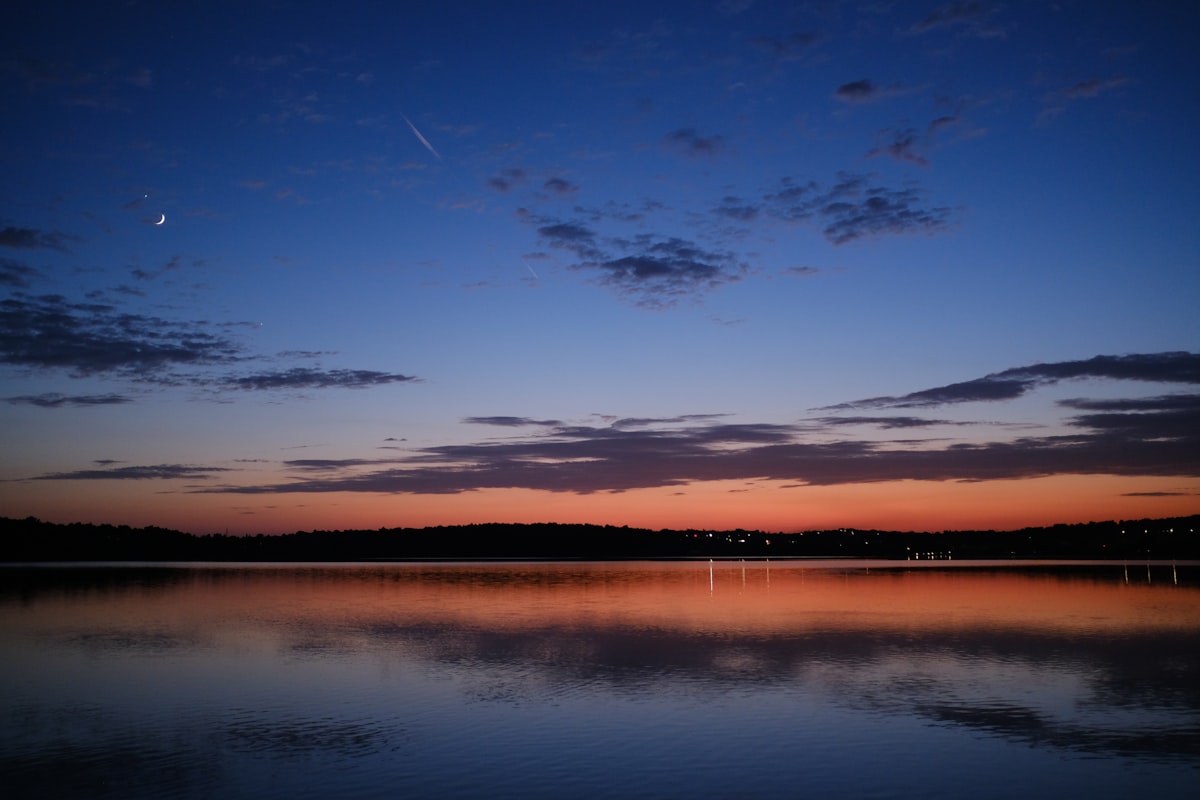 Calm lake at twilight beneath a crescent moon
